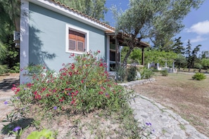 A house with a tiled roof, a window with shutters, and a garden with various plants and flowers.