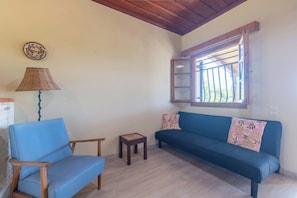 A living room with a blue sofa, a small wooden table, a lamp, and a window with a metal grill.