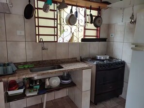 Cocina compacta con estufa a gas, un lavamanos y una ventana con ollas colgantes.