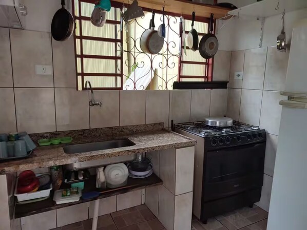 Een compacte keuken met een gasfornuis, een spoelbak en een raam met hangende pannen.