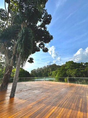 A wooden deck with a railing overlooking a body of water and dense greenery.