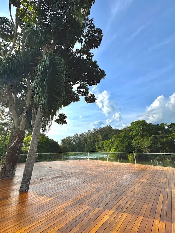 A wooden deck with a railing overlooking a body of water and dense greenery.