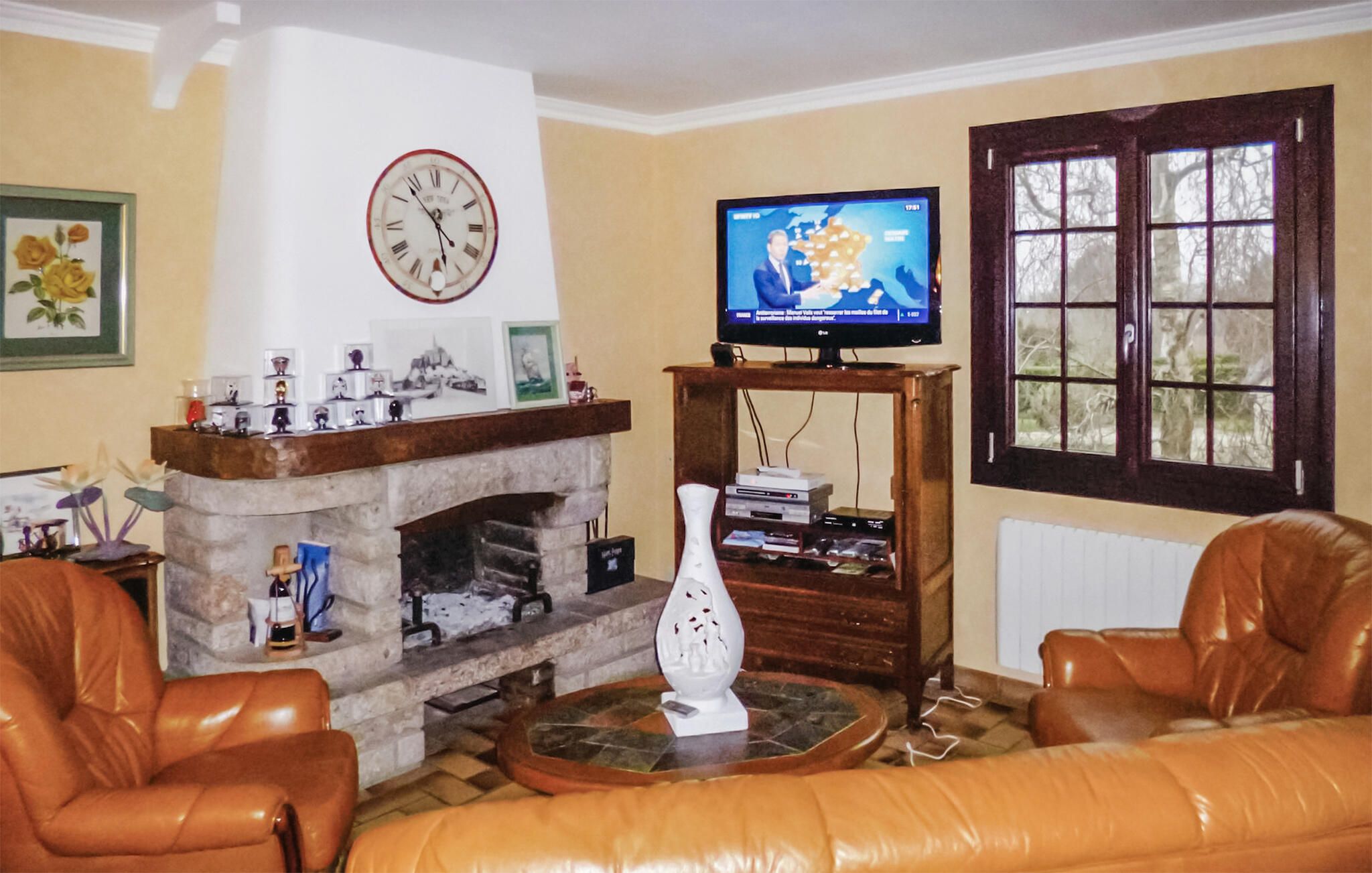 A living room with a fireplace, a television, leather sofas, and a clock on the wall.