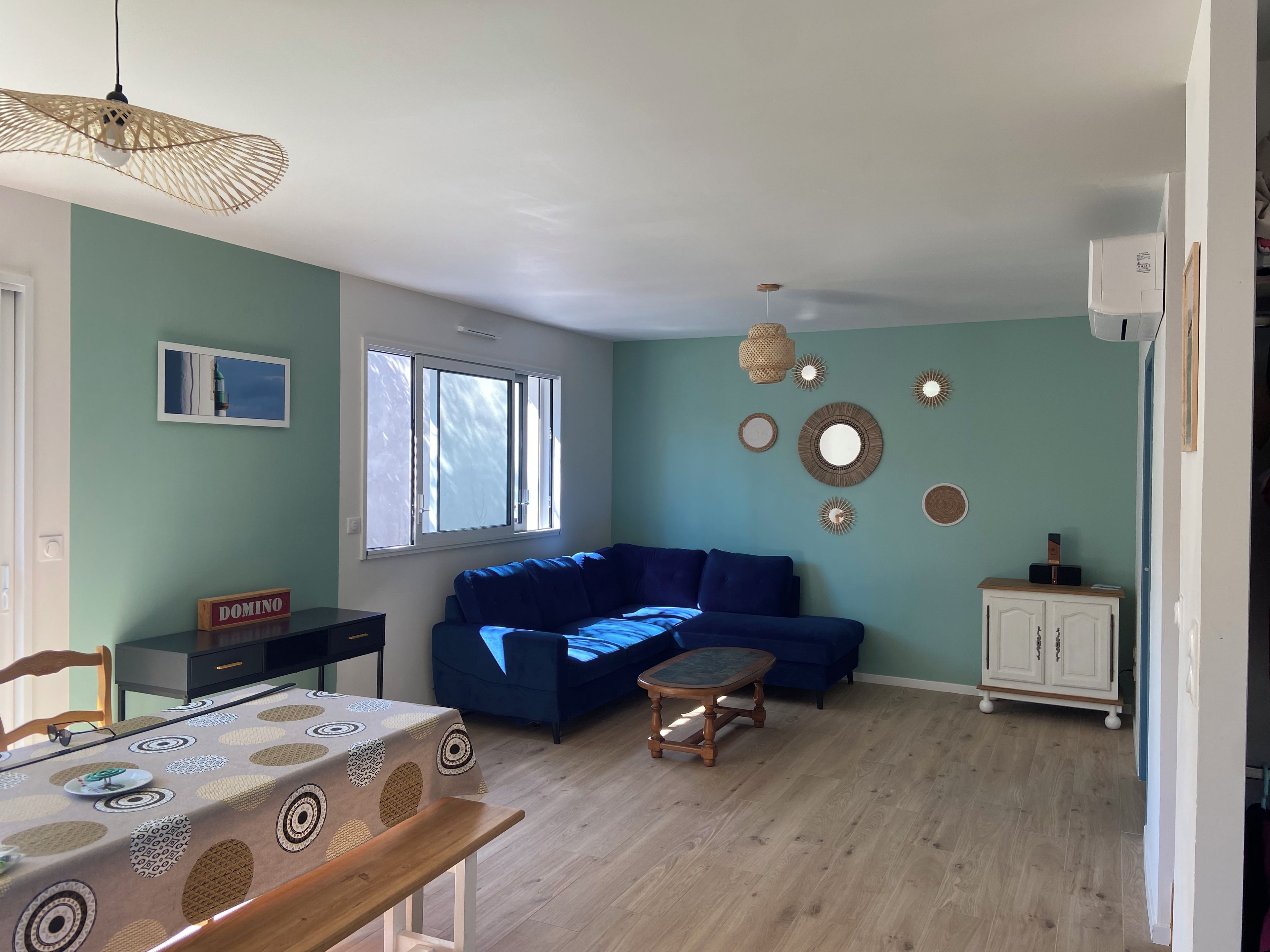 A living room with a blue sofa, a dining table with a patterned tablecloth, and a cabinet.