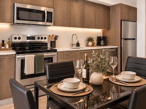 A modern kitchen with stainless steel appliances, wooden cabinets, and a dining area with a table set for two. - Modern Luxury Miami Apartment with Pool & Gym (Miami)