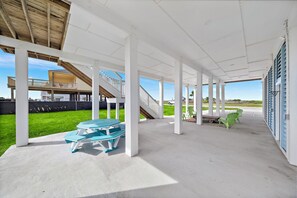 Un espace extérieur abrité, équipé d’une table de pique-nique et de chaises, d’un escalier et offrant une vue sur un immeuble d’habitation.