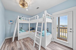 Une chambre avec des lits superposés, une porte donnant sur un balcon et un ventilateur de plafond.