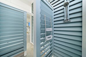 A hallway with a blue door and a white shelf unit with a showerhead. - Indian Beach | Decks, Views & Walk to Beach (Galveston)