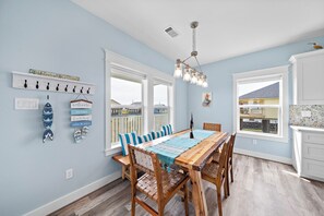 Un coin repas avec une table en bois, des chaises et une vue sur la plage grâce à de grandes fenêtres.