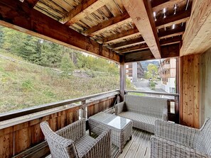 A wooden deck with wicker furniture and a view of a street and buildings. - Acoya - Les Gets - ski-in/ski-out (Les Gets)