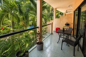 Ein Balkon mit Tisch und Stühlen, umgeben von üppiger Vegetation und Blick auf einen Pool.