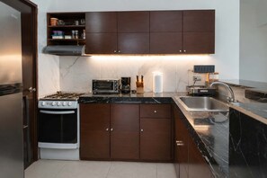A modern kitchen with dark wooden cabinets, a gas stove, a built-in oven, a coffee maker, and a sink. - 3BR Ground-Floor Condo with Pool & Terrace (Puerto Aventuras)