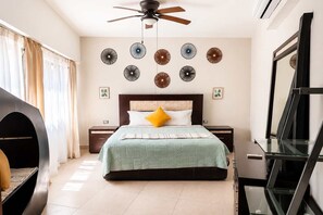 A bedroom with a bed, nightstands, a ceiling fan, wall decor, and a mirror. - 3BR Ground-Floor Condo with Pool & Terrace (Puerto Aventuras)
