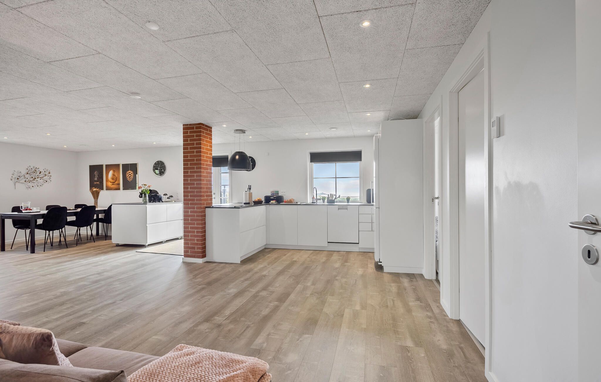 Une cuisine moderne avec des meubles blancs, une colonne en briques et une fenêtre.