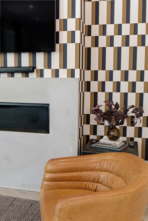 Een kamer met een geruit patroon op de muur, een wandtelevisie, een leren fauteuil en een tafeltje met een vaas en boeken.