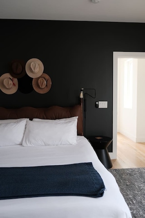 A bedroom with a bed, pillows, a dark wall, a nightstand, a lamp, and a door. - Downtown Rooftop Sleeps 10 Near Gulch and 12 South (Nashville)