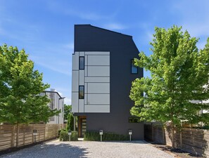 Ein modernes, zweistöckiges Gebäude mit Flachdach, großem Fenster im zweiten Stock und Auffahrt mit Kies.