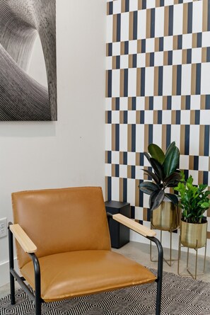 Ein modernes Interieur mit einem braunen Ledersessel, einer Wand mit geometrischem Muster und zwei Blumentöpfen.