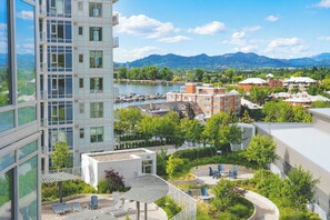 Un edifici modern amb una zona de terrassa a la teulada, vistes a un riu i vegetació al voltant.