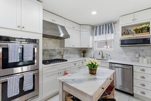 A modern kitchen with white cabinetry, stainless steel appliances, and a marble countertop. - Sleeps 12 - Dog-Friendly Nashville Cottage (Nashville)