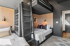 Une chambre à coucher moderne avec un lit superposé, une échelle, une table de chevet et un luminaire fixé au mur.