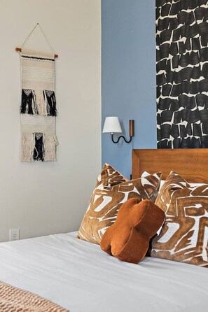 A bedroom with a bed, patterned pillows, a wall-mounted lamp, and a macramé wall hanging. - Luxury Nashville Urban Cowboy Rooftop | Sleeps 10 (Nashville)