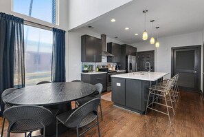 A modern kitchen with dark cabinetry, a central island, and a dining area with wicker chairs. - Luxury Nashville Urban Cowboy Rooftop | Sleeps 10 (Nashville)