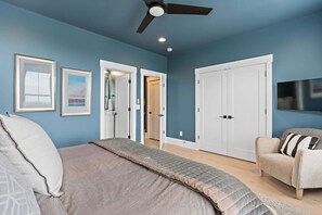 Un dormitorio con cama, una silla, armario y ventilador de techo.