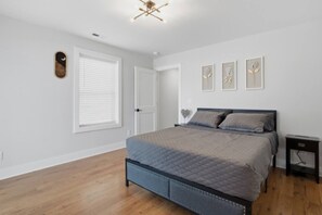 Ein Schlafzimmer mit einem Bett, einem Nachttisch, einer Tür und einem Fenster mit Jalousien.