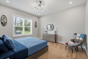 Een slaapkamer met een bed, kaptafel, stoel en een raam met jaloezieën.