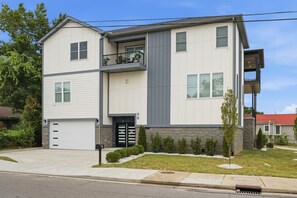 Een woonhuis met twee verdiepingen, een garage, een balkon en een keurig onderhouden gazon.