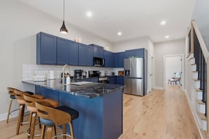 A modern kitchen with blue cabinets, a stainless steel refrigerator, and a bar area with stools. - WeHo 8BR Retreat | Two Homes, Room for 24 (Nashville)
