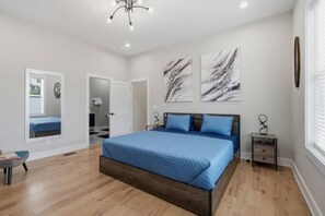 A bedroom with a large bed, a bedside table, a mirror, and a door leading to another room. - WeHo 8BR Retreat | Two Homes, Room for 24 (Nashville)