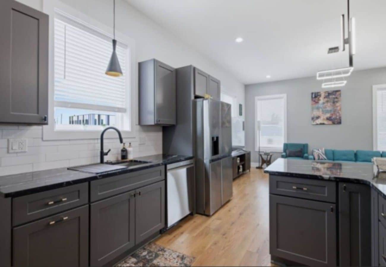 A modern kitchen with dark cabinetry, a stainless steel refrigerator, and a black countertop.