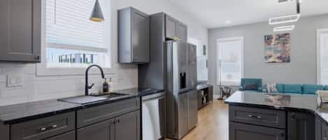 A modern kitchen with dark cabinetry, a stainless steel refrigerator, and a black countertop.