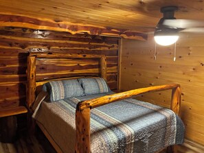 Un letto di legno con testiera, un comodino e una ventola a soffitto.