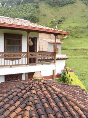 Una casa con techo de tejas, un balcón con barandilla y un jardín lleno de flores.