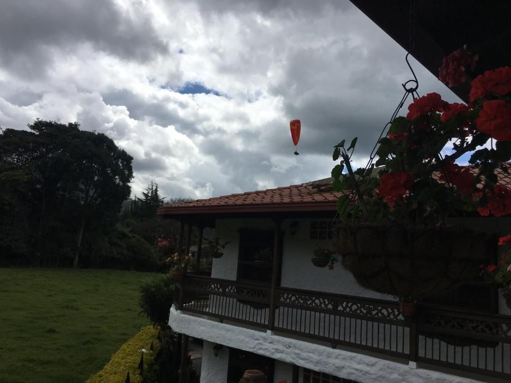 Een huis met een balkon, een tuin en een luchtballon aan de hemel.