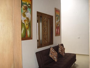 Una habitación con un sofá marrón oscuro, dos cojines estampados, una puerta de madera y dos cuadros en la pared.