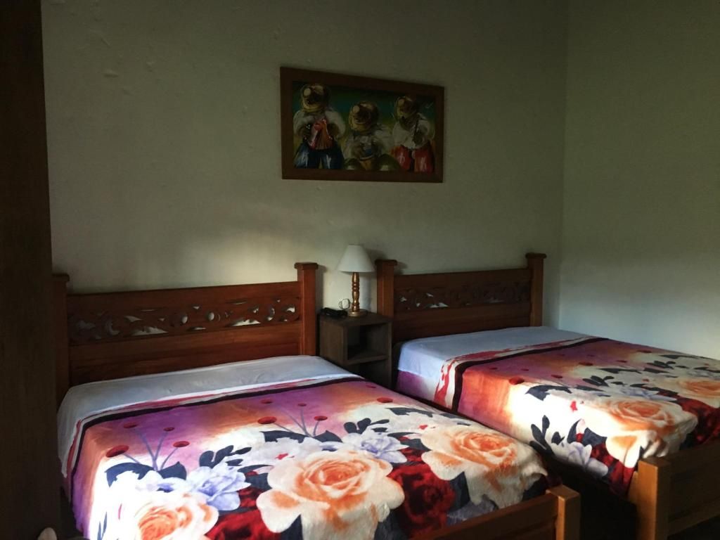 A room with two wooden beds, each with a floral bedspread. There is a painting on the wall above the beds.