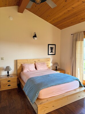 A bedroom with a wooden headboard, a bed with pink and blue bedding, two bedside tables with lamps, a wall-mounted light fixture, and a framed picture. - Spacious and secluded ranch getaway on 200 acres (Grass Valley)
