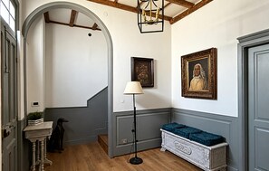 Ein Flur mit einer Treppe, einer Lampe, einer Bank und zwei gerahmten Porträts an der Wand.