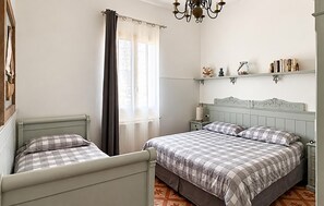 Ein Schlafzimmer mit zwei Betten, einem Fenster mit Vorhängen, einer Kristallleuchtre und einem Regal mit Büchern und Dekoration.