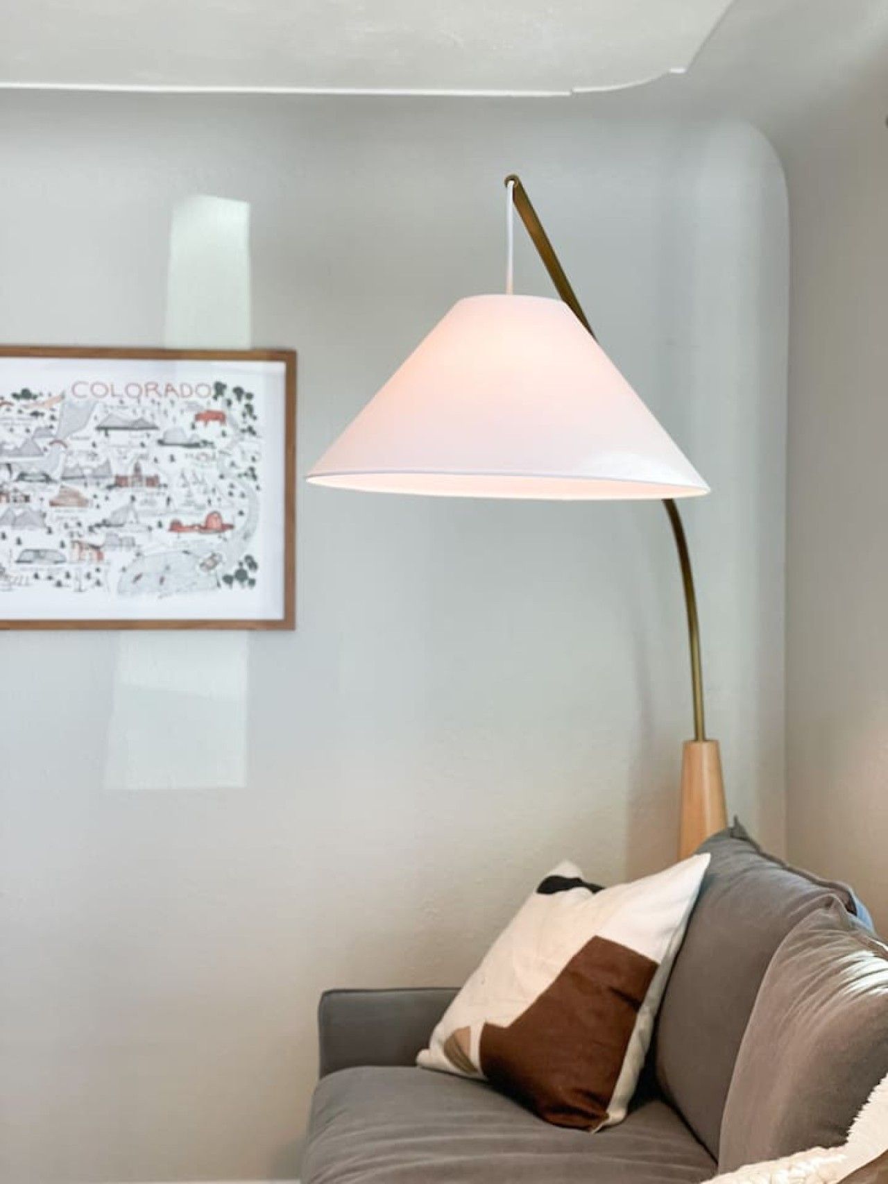 Une pièce avec un canapé gris, une carte du Colorado encadrée et une lampe avec un abat-jour blanc.