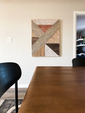A dining area with a wooden table, a black chair, and a wall-mounted abstract artwork.