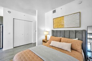 A modern bedroom with a large bed, a nightstand, a lamp, and a wall-mounted artwork. - High Rise Ocean View Downtown Miami (Miami)