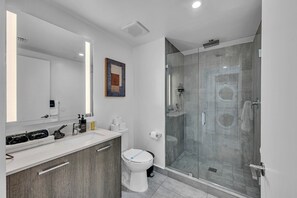Une salle de bain moderne avec une douche à parois de verre, des toilettes blanches et un meuble-lavabo doté d’un miroir et d’un évier.