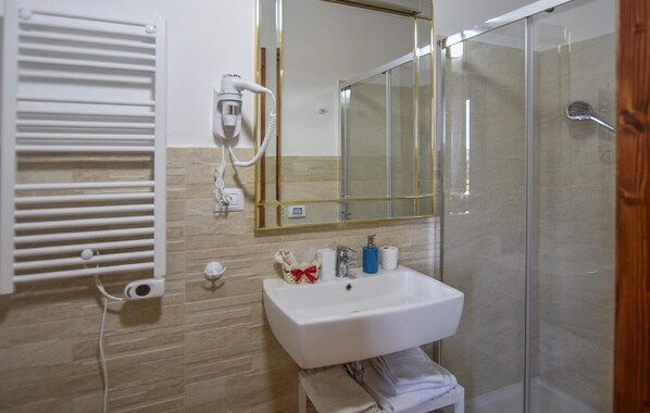 Une salle de bain avec un lavabo blanc, un miroir, un porte-serviettes et une cabine de douche en verre.