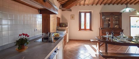 Une cuisine avec un mur recouvert de carreaux, des meubles en bois, un coin repas avec une table dressée pour deux personnes et une fenêtre laissant entrer la lumière naturelle.