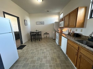 A compact kitchen with a refrigerator, microwave, oven, and sink. There is a dining table with chairs and a small plant on the wall. - The Downtown Hideaway – Stylish 1BR Comfort (Greensboro)